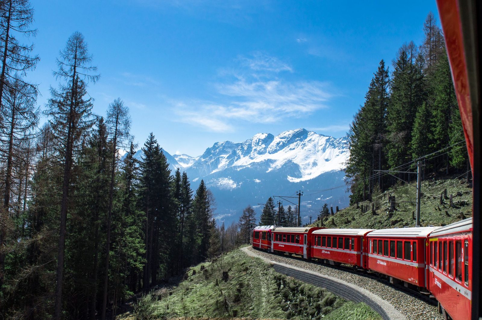 Red Rhaetian Railway train in front of snow-covered Alps